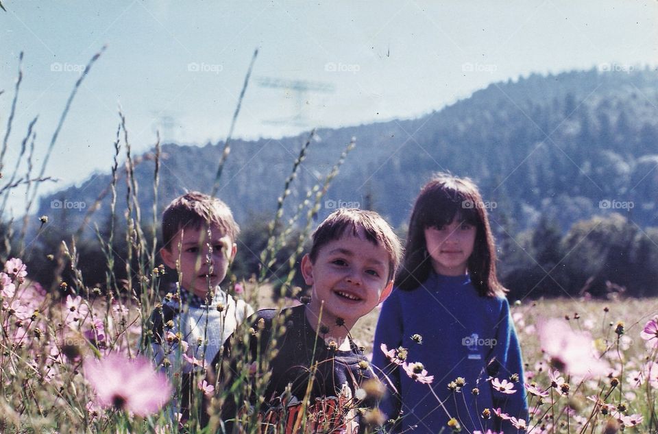 3 childs playing in a flower field with a mountain as a background.