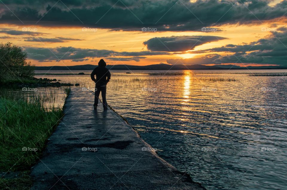 Beautiful sunset scenery with silhouetted man on the dock watching sunset at Corrib lake in Galway ,Ireland