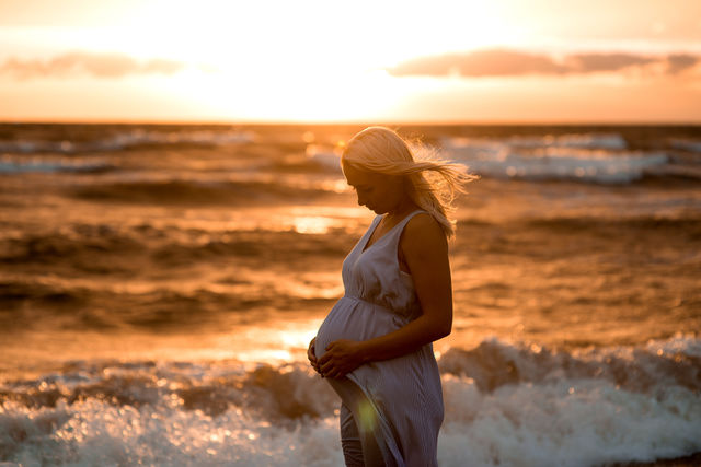 Pregnancy, rest, people and expectation concept- happy pregnant woman touching her belly at sea during sunset