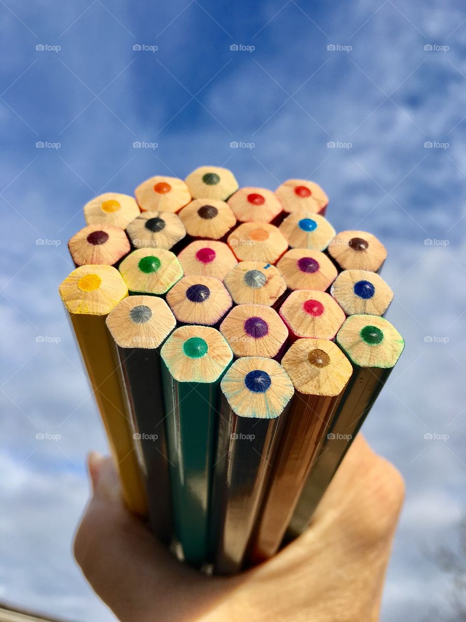 Person's hand holding colored pencils against sky