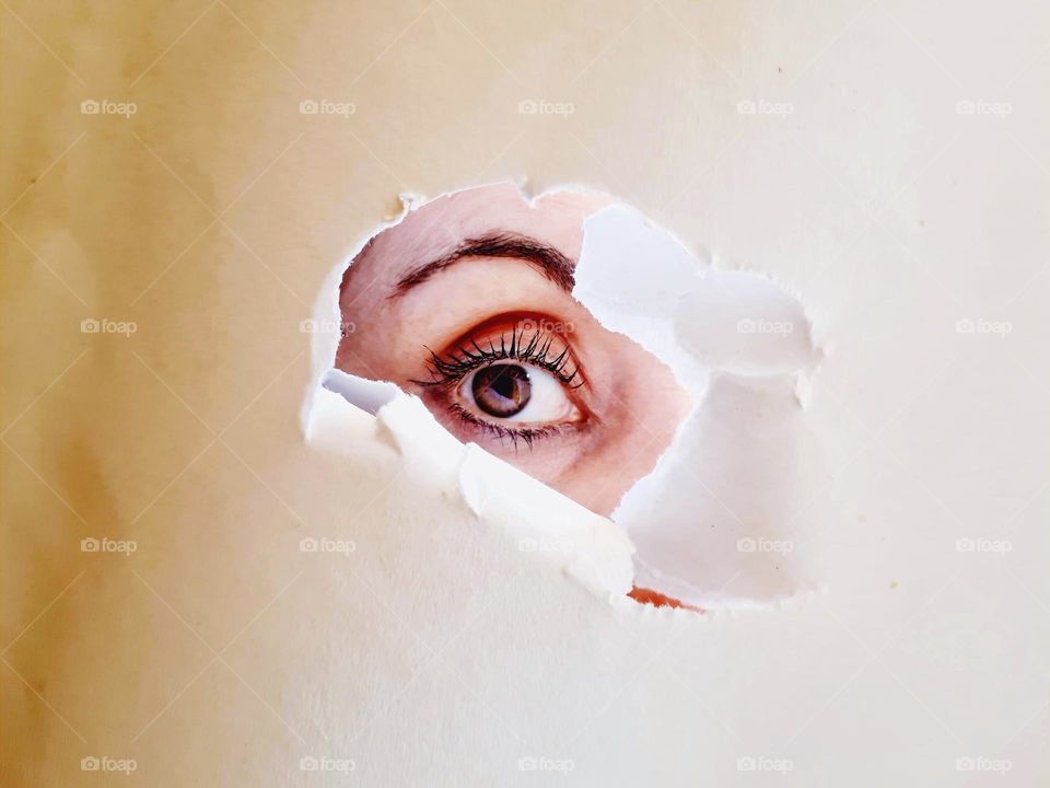 detail of female eye with makeup behind a torn cardboard
