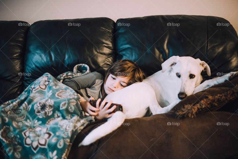 Little boy laying down on top of his phone using a phone 