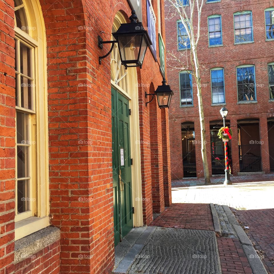 Lamp posts around the green door in Salem, Massachusetts. The building is reddish brick and a lamp post with holiday decorations on it can be seen in the background.