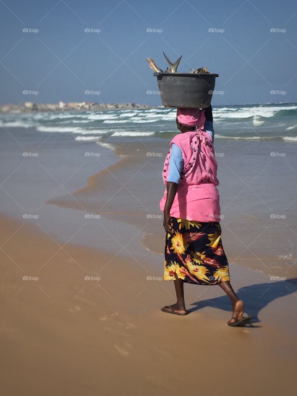 Woman carrying  fish in a bucket on her head.