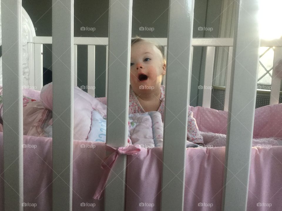 Baby with Down syndrome looking through crib slats