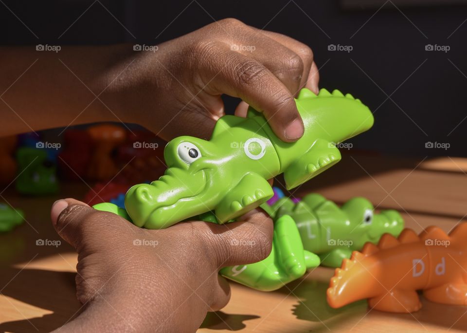 An african American 5year old child holding a green alphabet crocodile toy in his hands