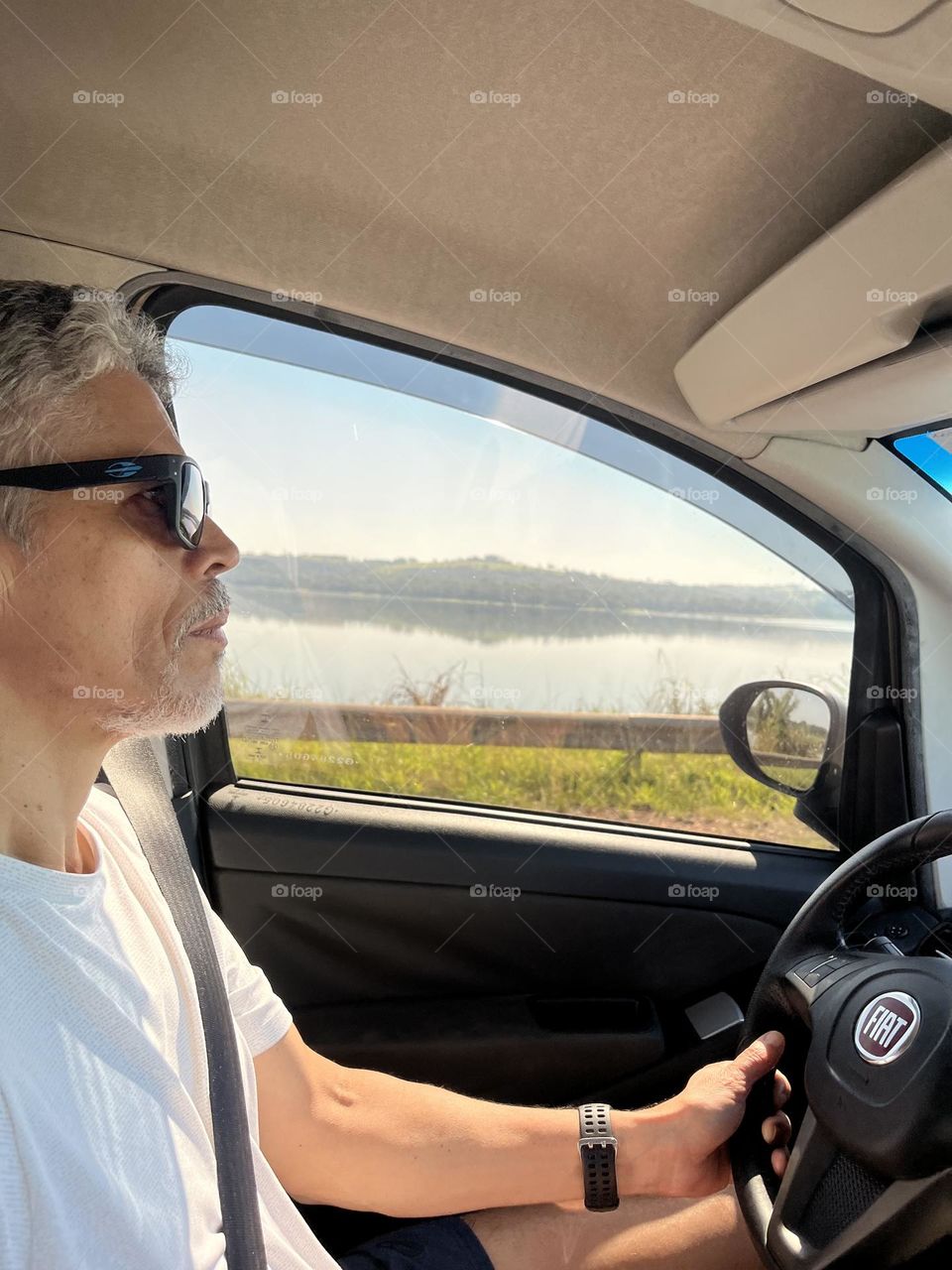 A man profile driving a car, wearing sunglasses Water background