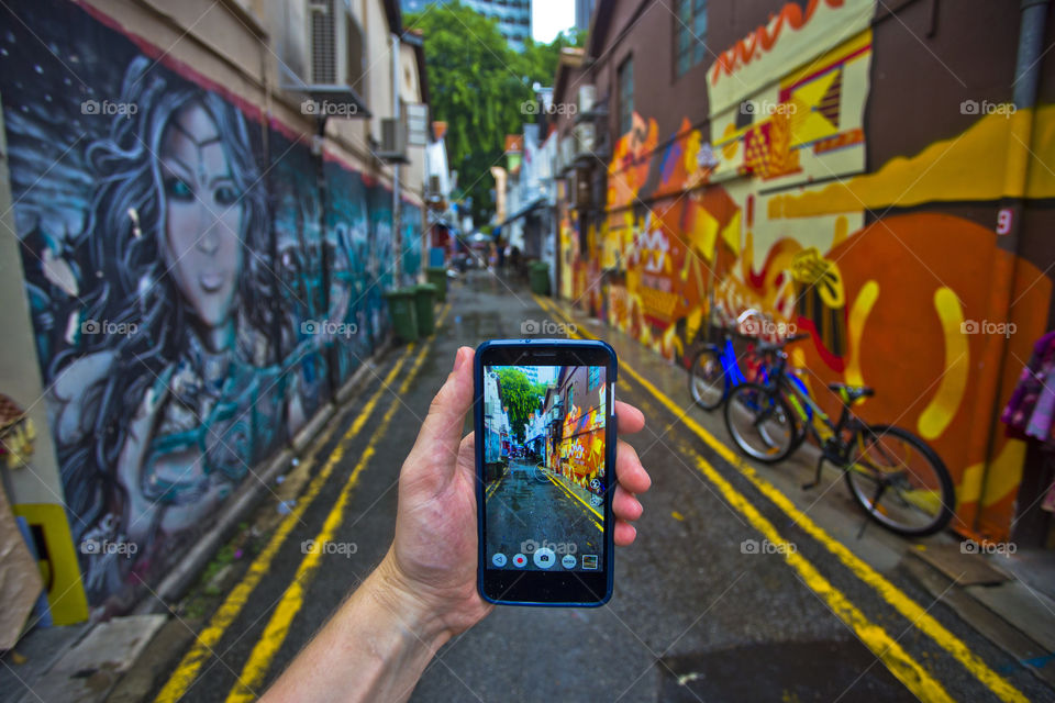 first person view point hand holding mobile phone taking picture of street art graffiti colorful paint in Haji Lane Singapore
