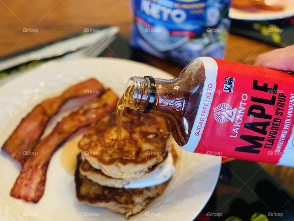 Pouring maple syrup over pancakes with a side of bacon