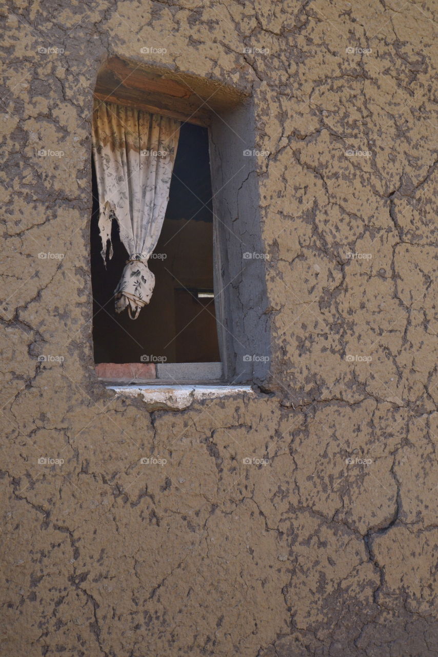 A traditional Basotho house. The outside look of a window with torn curtains and a cracked mud-wall.