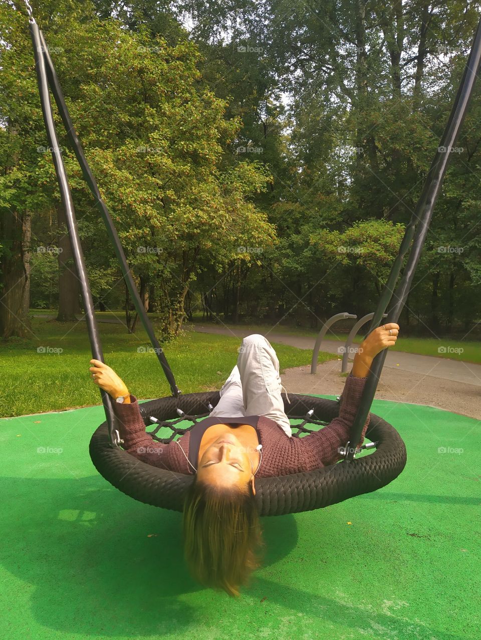 A park.  Sunny day.  A woman lies on a suspended swing and smiles at the sun, in harmony with nature