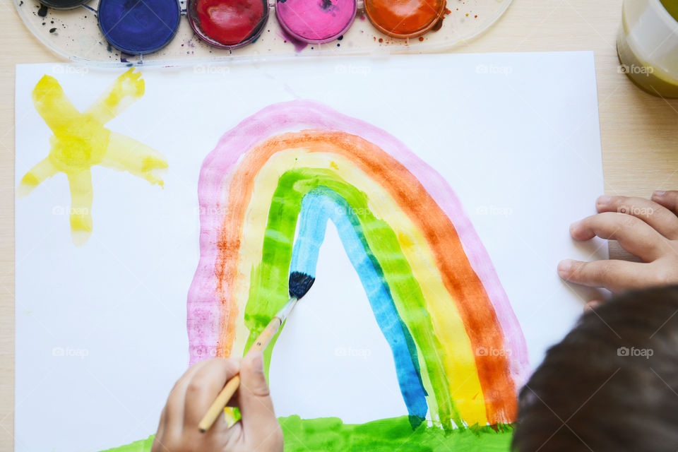 Kid drowing rainbow by watercolors. Top view