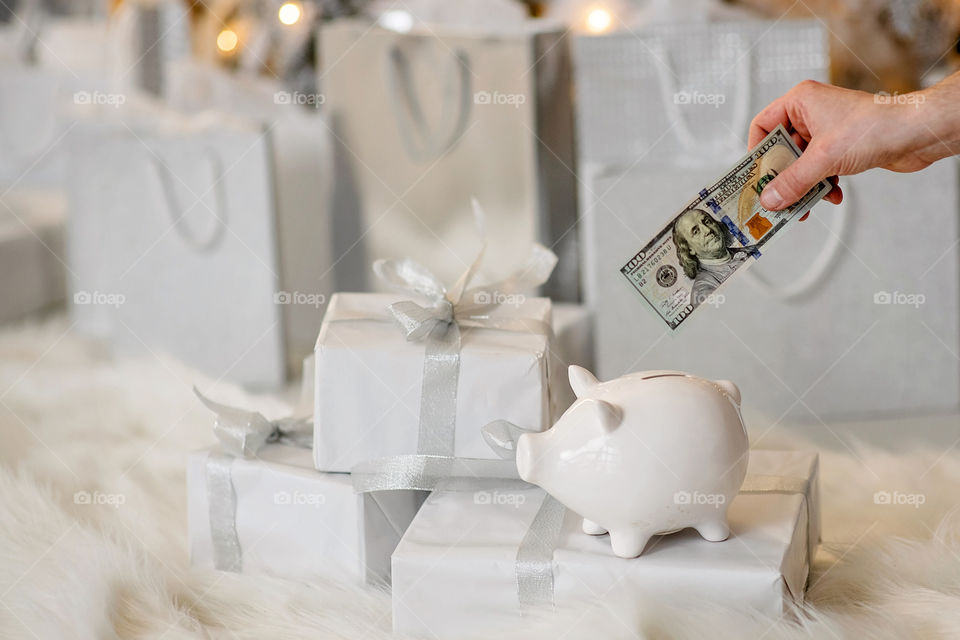 piggy bank with 100 dollars banknote in festive New Year atmosphere of scenery.  Magical bokeh with Christmas tree and bright lights.