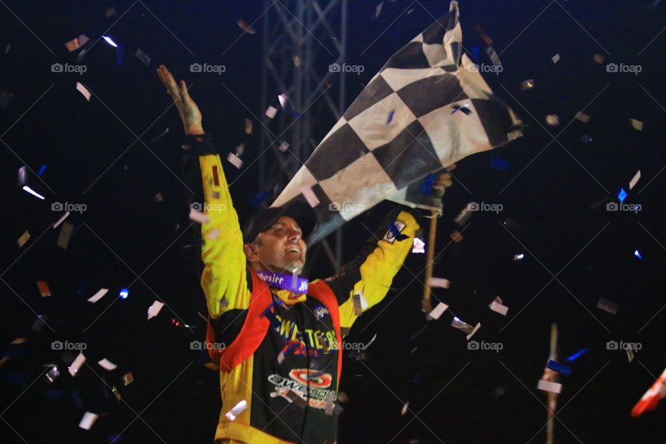 Race Car Diver Celebrates in Victory Lane while waving a checkered flag 