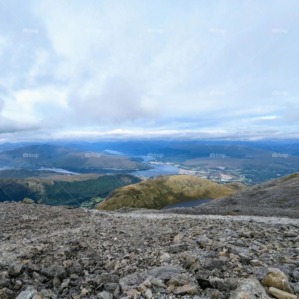 view from a mountain. the stone path in the foreground and land looking small in the background (below). clouds overhead