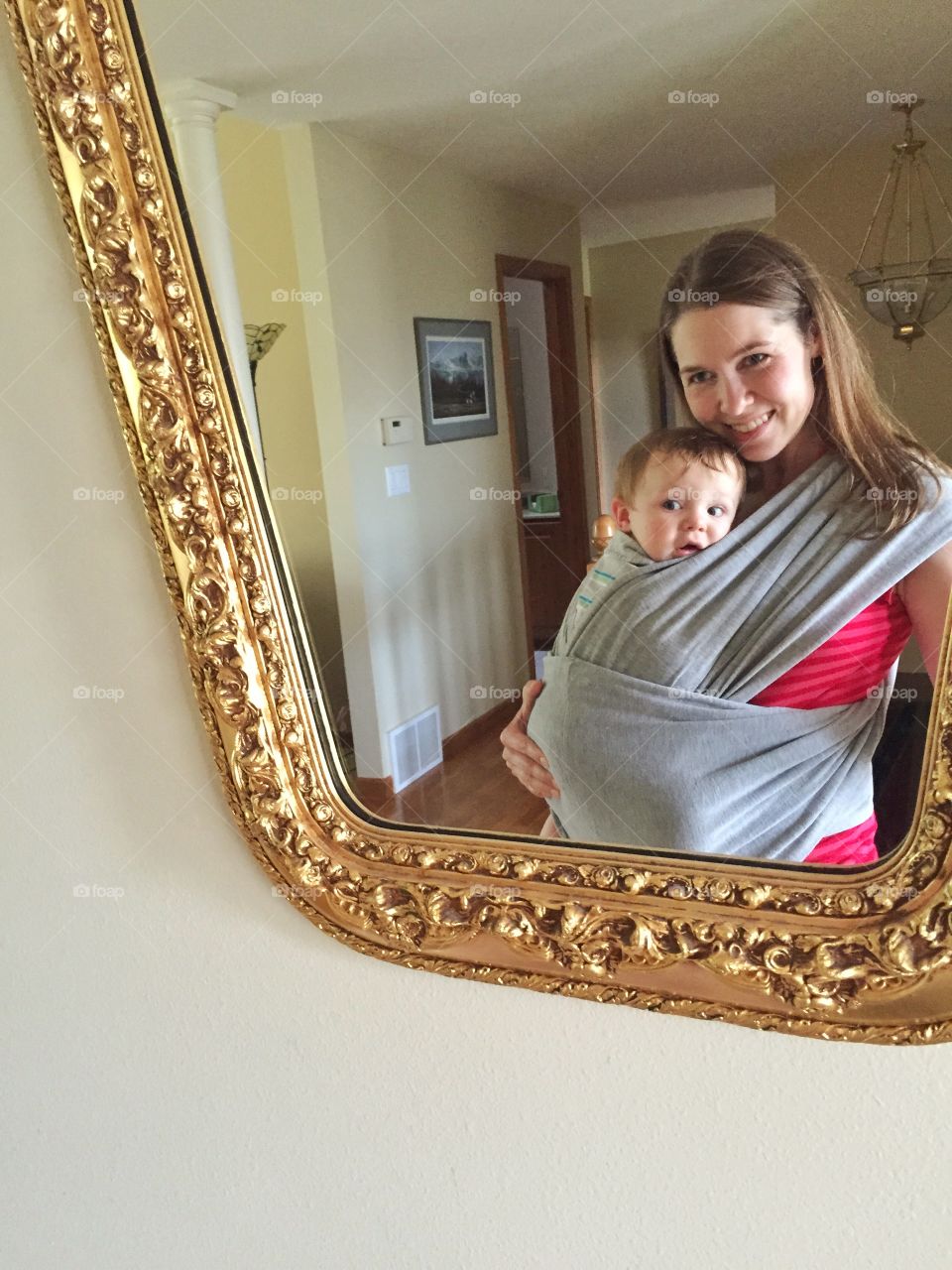 Reflection of mother carrying her cute baby boy in sling