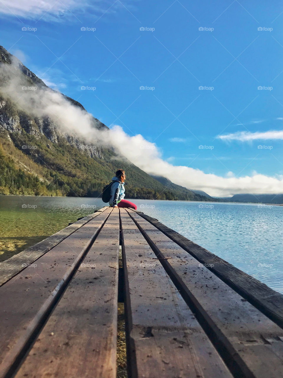 Woman traveler sitting at the wooden bridge near big lake Bohinj at her autumn trip in Alps, Slovenia. Foggy landscape.