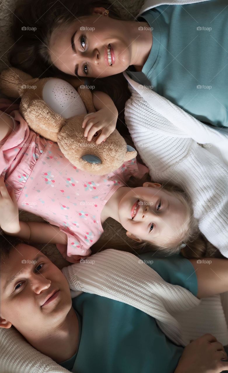 Cheerful family lie on the floor looking at the camera. parents and daughter