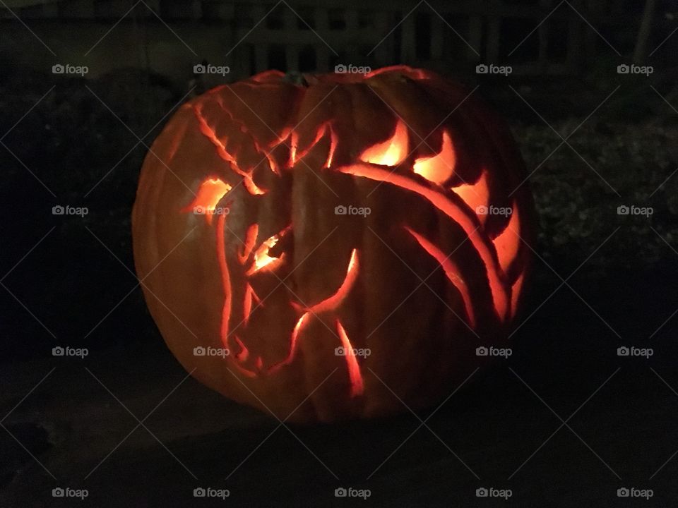 Fierce unicorn carved pumpkin lit with a candle, sitting in the dark