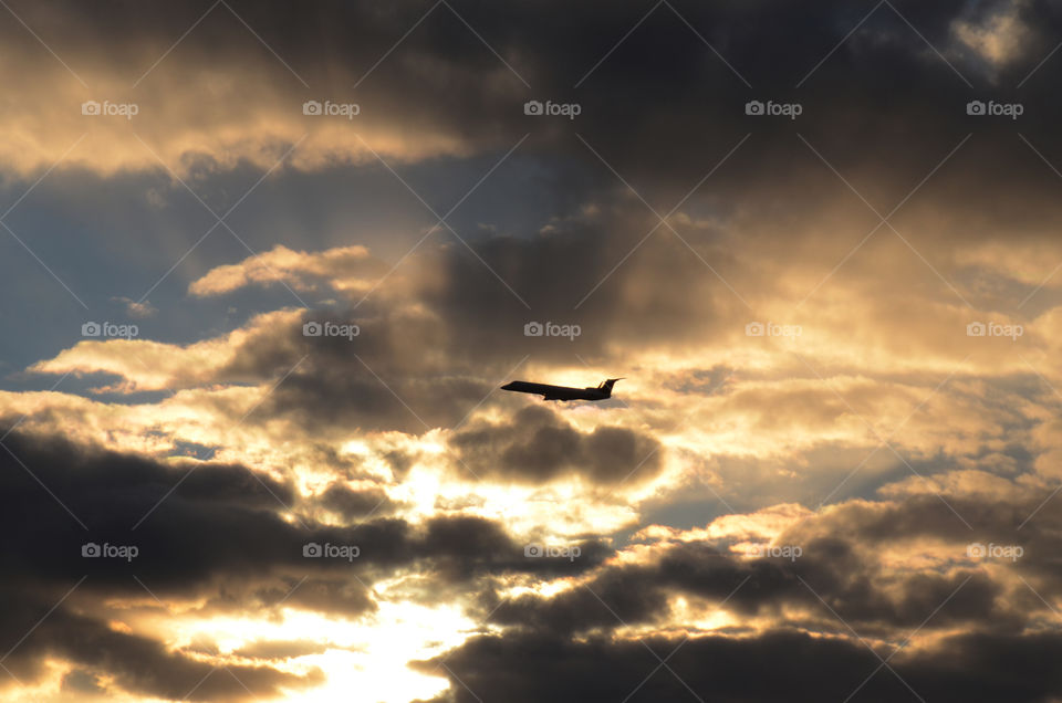 A silhouette of commercial jet is seen crossing the face of a beautiful cloudscape luminated by a pretty evening sunset.