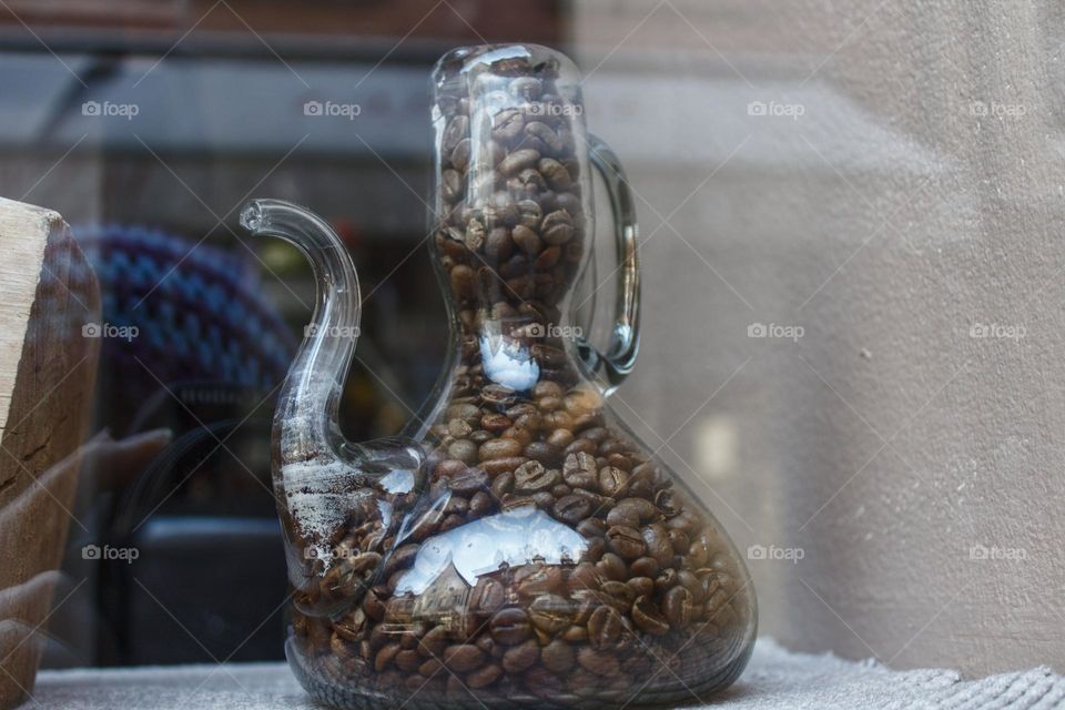 Glass carafe with coffee beans, reflections on the glass of the surroundings and a reflection of the photographer in the window.