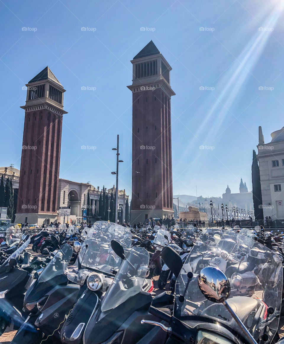 Rows on motorcycles are parked up in front of the Venetian towers at Plaça d’Espanya on a sunny spring day