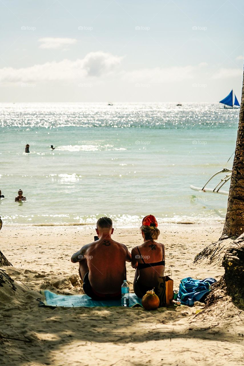 A couple from behind while relaxing at the beach under the heat of summer