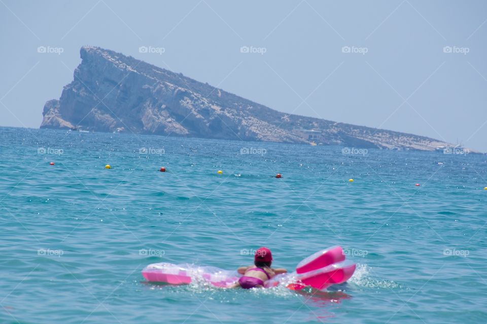 Little girl relaxing on an air bed in the ocean in benidorm with a view on a huge rock