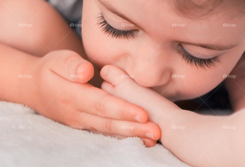 Portrait of one beautiful little Caucasian girl kissing her newborn sister's foot while lying on the bed during the day, close-up side view.