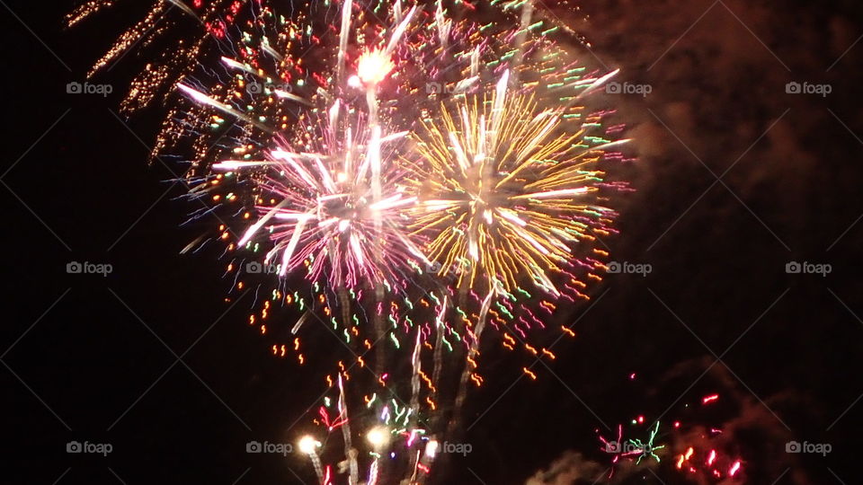 Celebration fireworks multicolor bursts pink gold red orange green against black night sky