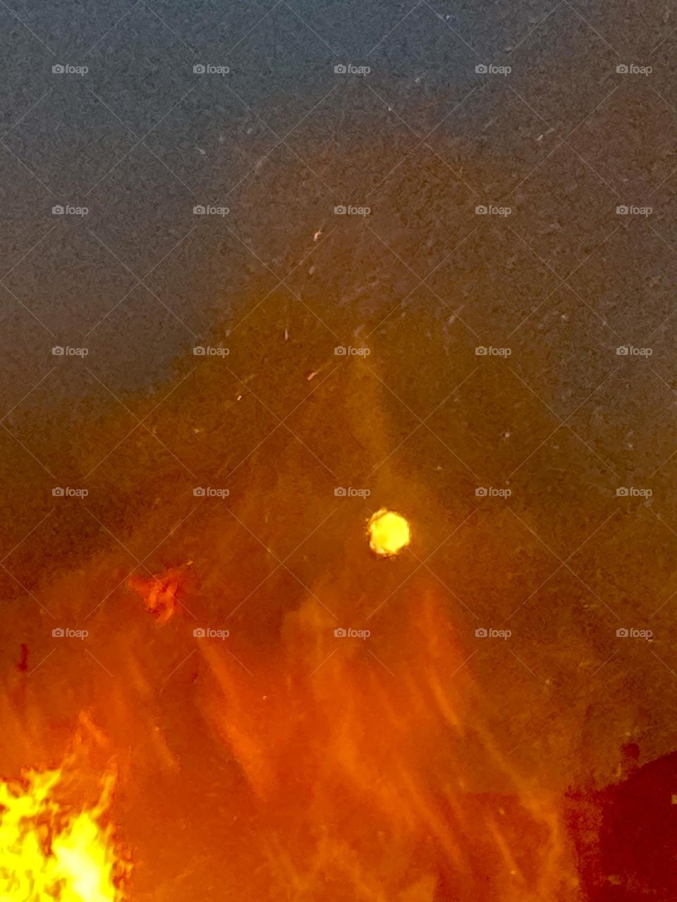 The full moon is filtered through the flames of a bonfire on a chilly autumn evening.