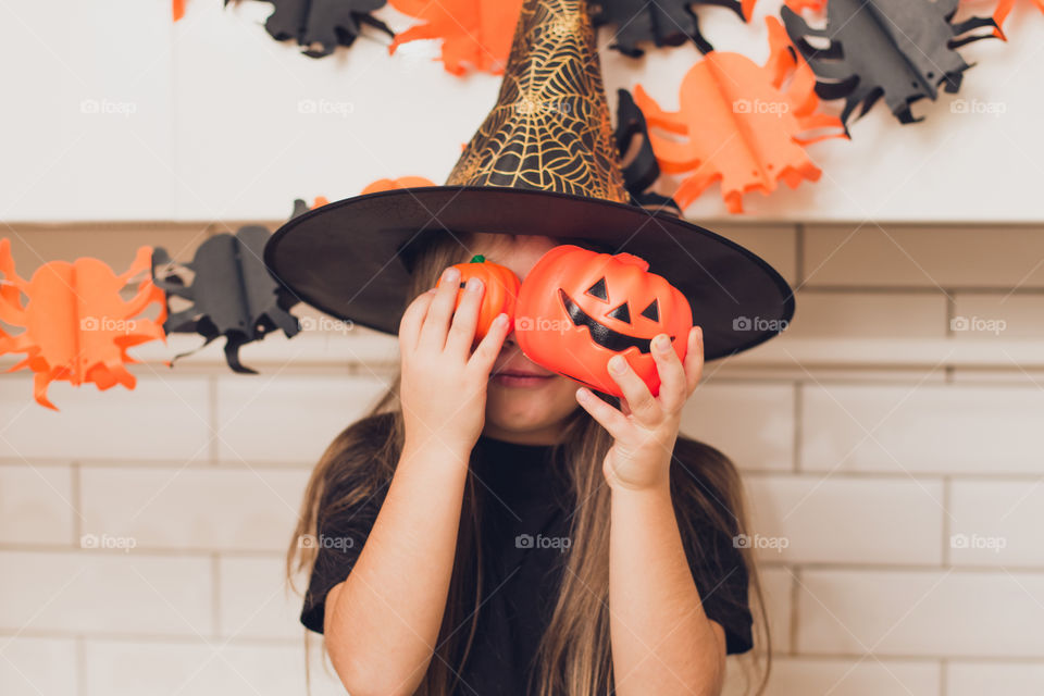 Little girl dressed as a witch for halloween holding a pumpkin with a face on the background decor