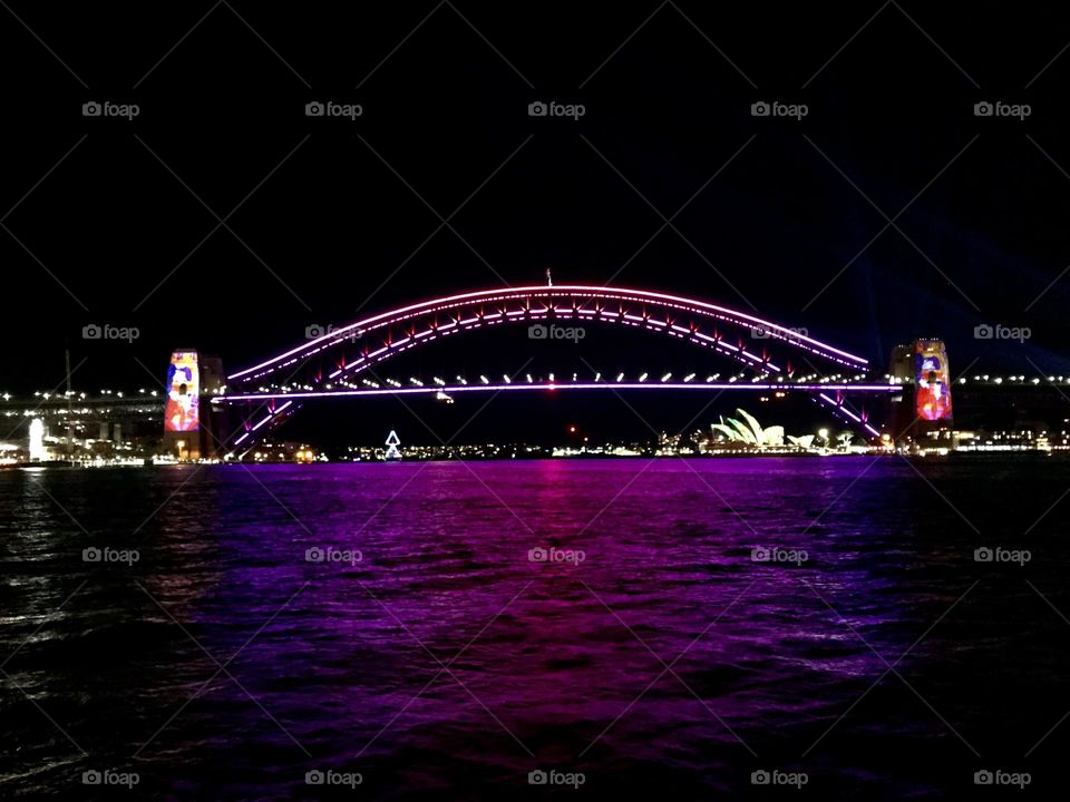 A beautiful camera click of the Sydney Harbour Bridge from a distance in magenta colour during vivid Sydney.