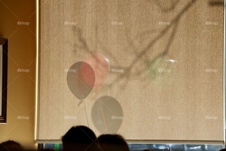 People celebrating, heads together and shades of balloons and tree branch on the window screen 