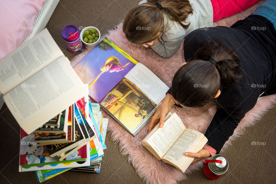 Parent and child reading books with stack of books in bedroom. Image from above of books and reading together. Staying in good shape mentally by sticking to good habits. Fresh fruit and water as healthy snacks keeping a healthy lifestyle.
