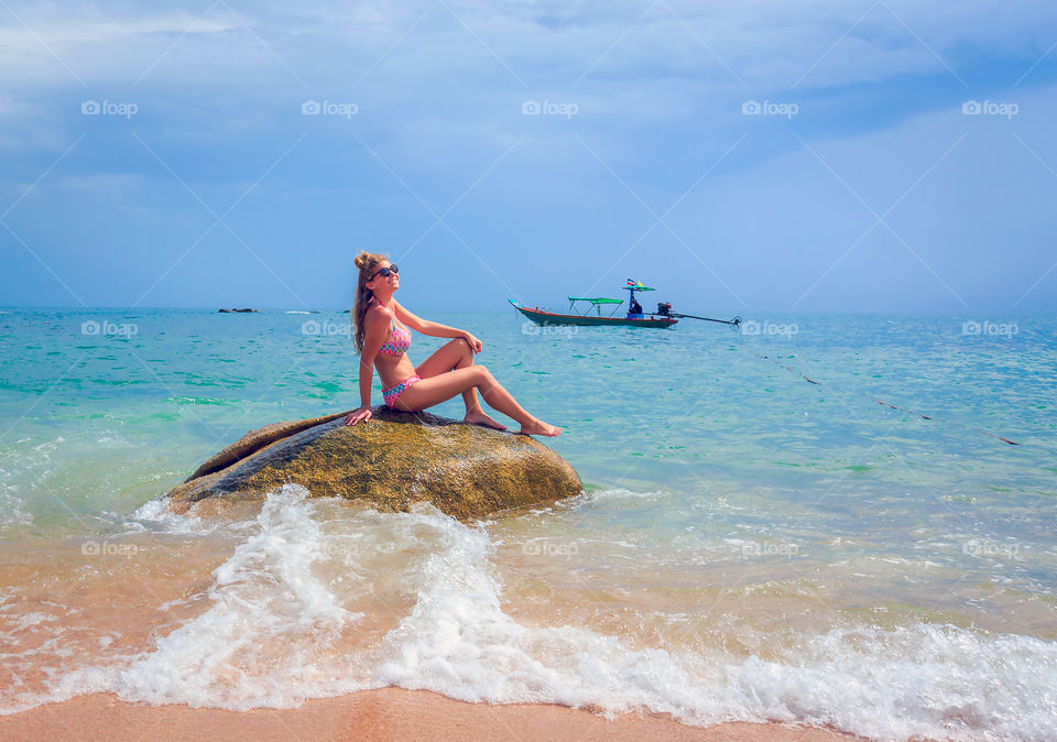 Young woman in bikini sitting on rock in sea