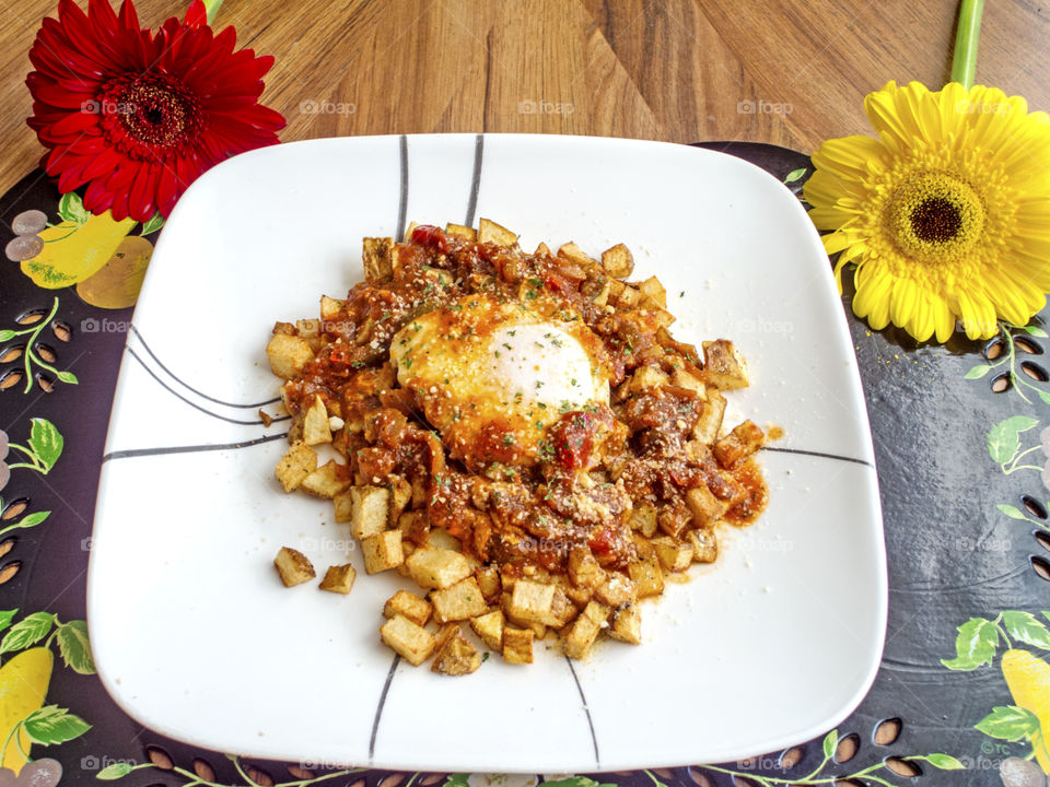 Closeup of poached egg on fried potatoes with tomato sauce