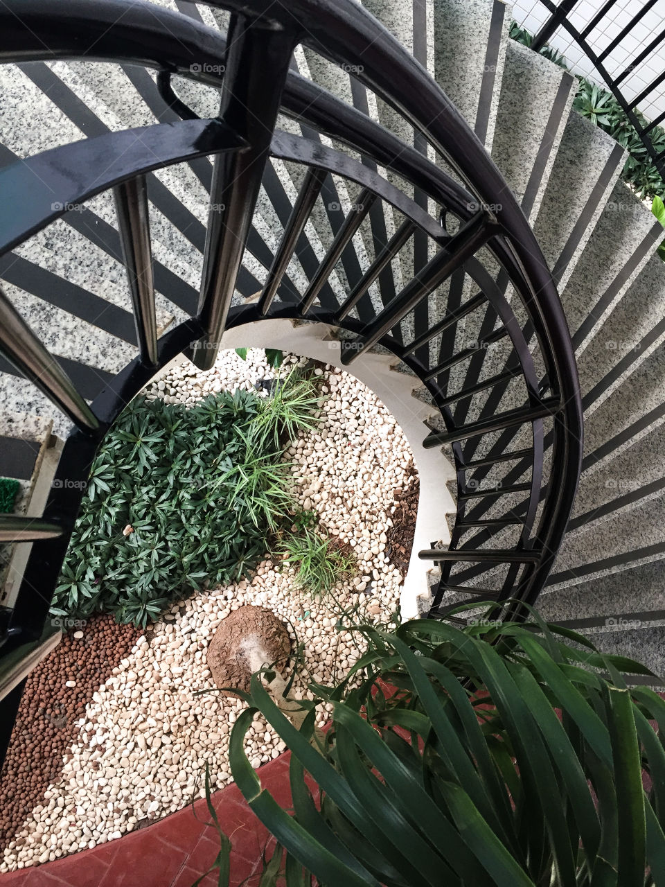 Spiral staircase over internal garden with decorative stones and foliage.