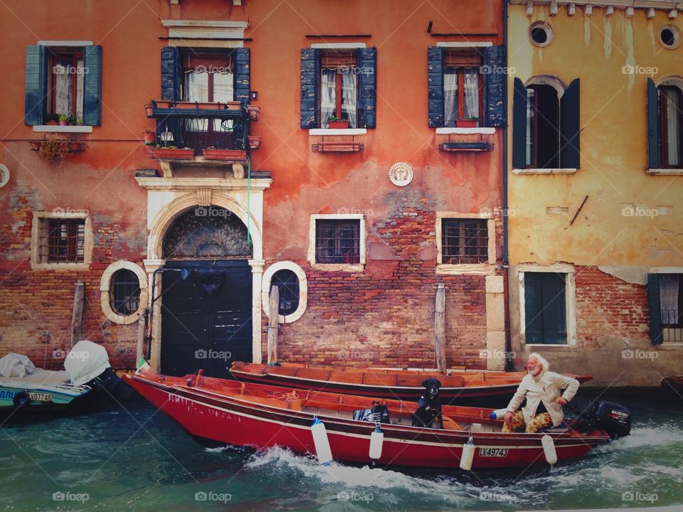 Smiling grey haired man with his dog-friend enjoying the moment sitting in gondola, in Venice channel. 