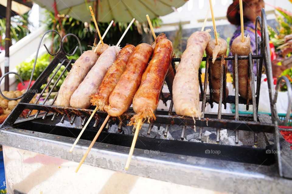MUKDAHAN, THAILAND -APR 24, 2011 Thai Sausages are grilled on charcoal stove. Prepared for sale to tourists visiting the lndochina market. Mukdahan, Thailand.