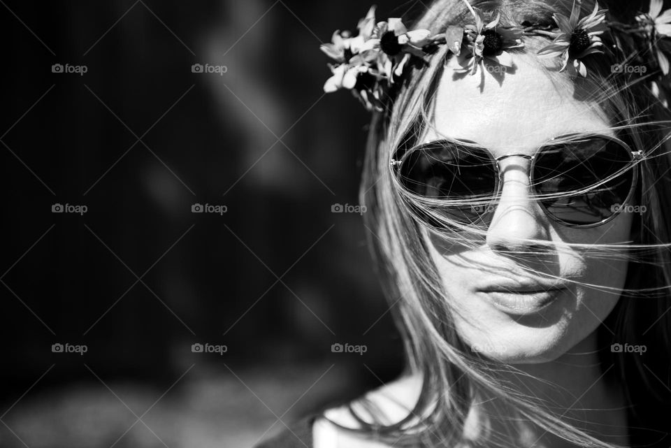 Black and white portrait of a millennial woman wearing a flower crown and retro sunglasses 