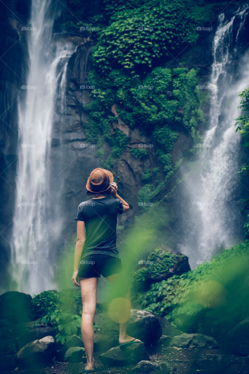 Girl in a straw hat stands on the background of a waterfall. Bali island.