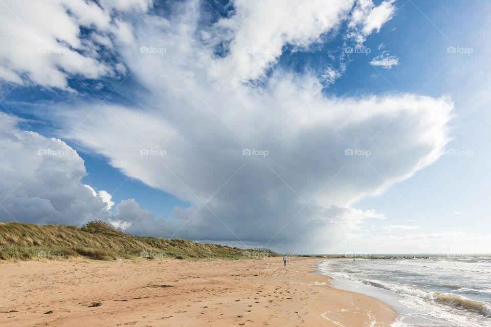One man walking alone on the sand beach by the ocean under a big cloud formation 