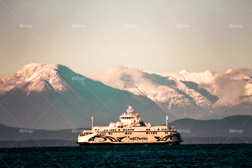 A British Columbia ferry during its crossing between the island & the mainland. Wispy clouds danced between the peaks as the setting winter sun kissed the snow covered mountains & the ferry glowed golden on the deep turquoise blue waters.