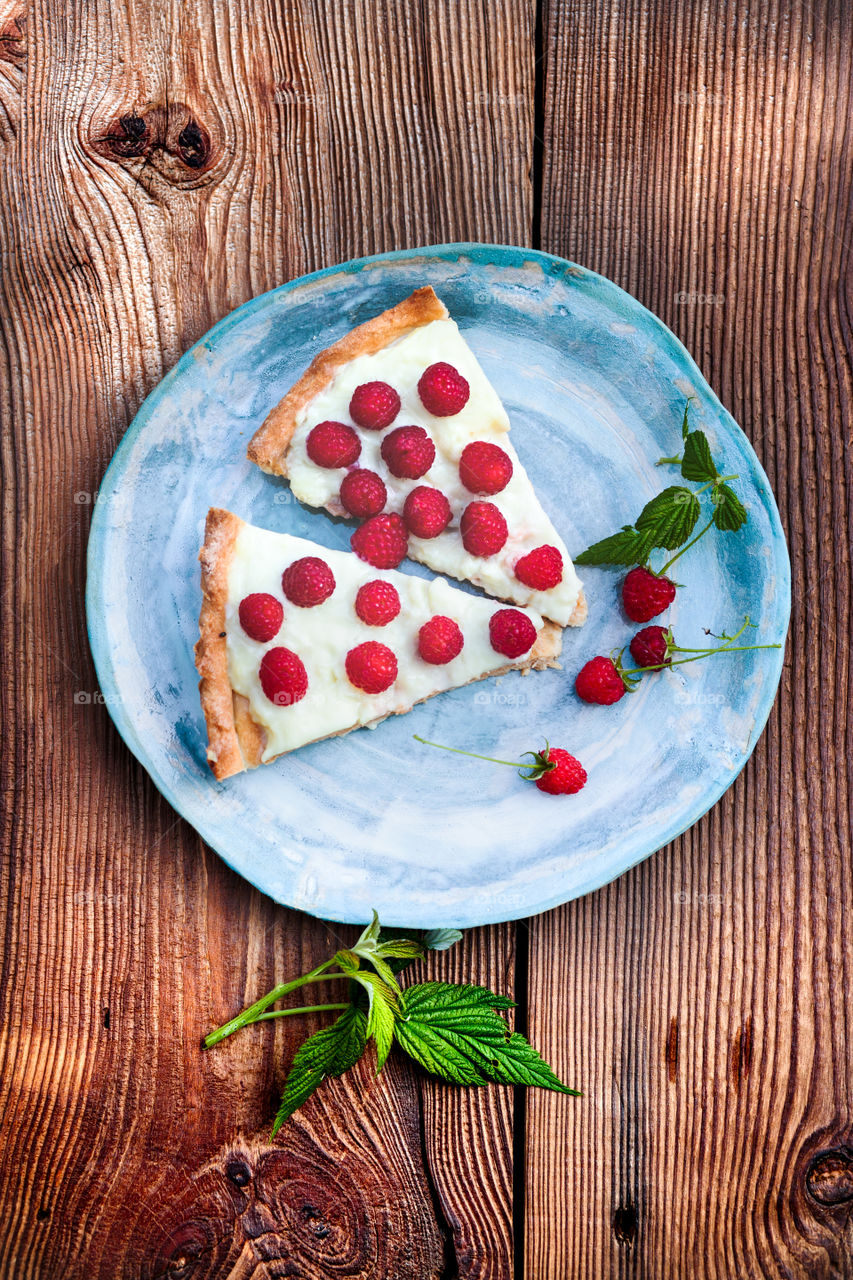 Home cake with pudding and fresh raspberries on blue handmade pottery plate on old wooden table from above