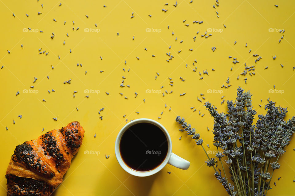 Business working morning with cup of hot coffee, sweet croissant, lavender flowers on yellow background close up. Top view, copy space, flat lay, mockup.