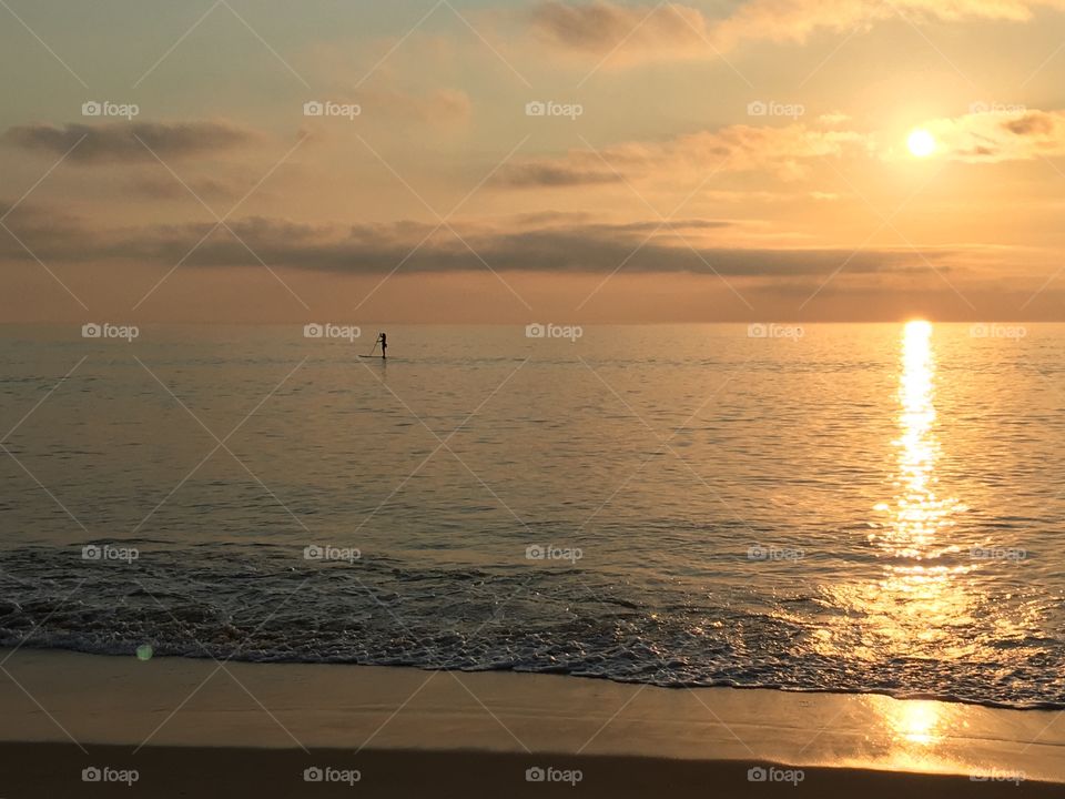 Sunrise at the beach with paddle boarder silhouette. 