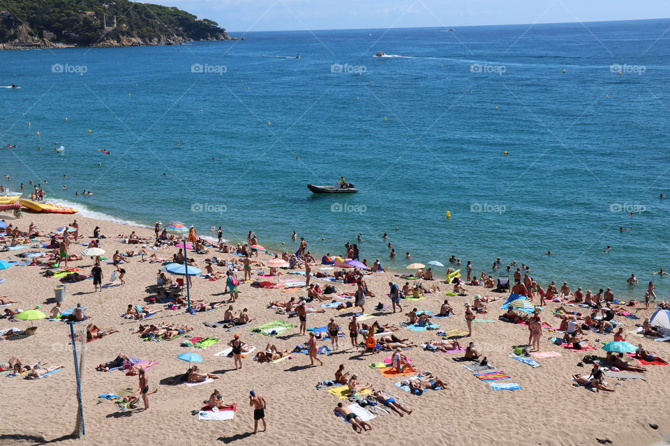 Sandy beach crowded with people sunbathing, relaxing or swimming in the warm sea - enjoying the summertime 