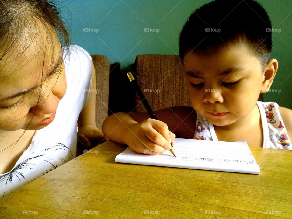 Little boy learning to write and supervised by parent