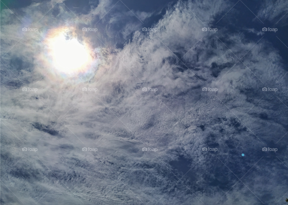 The sun hides behind wispy, white clouds on a beautiful summer day.